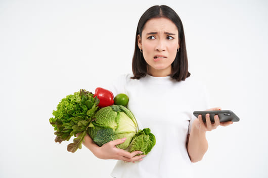 portrait young woman holds vegetables organic food holds smartphone with concerned worried face i11